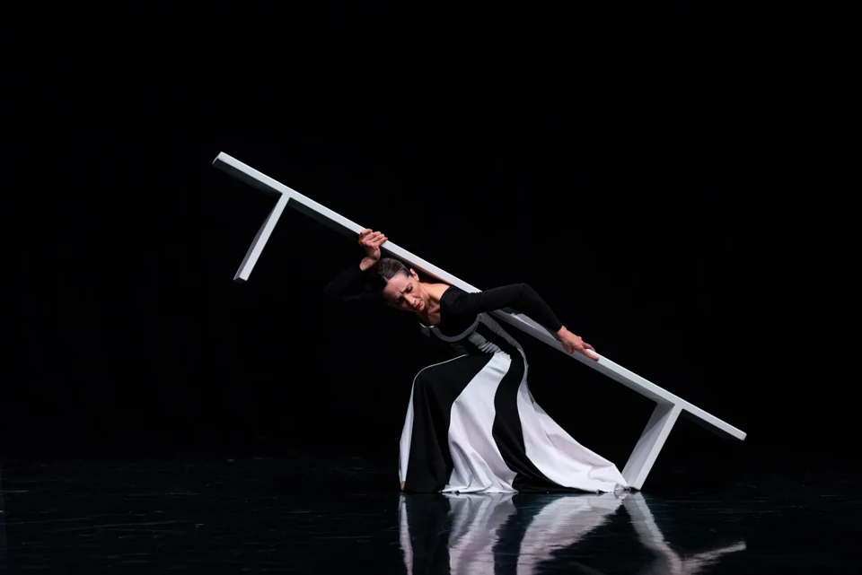 Amy Thake carrying a white bench across a dark stage