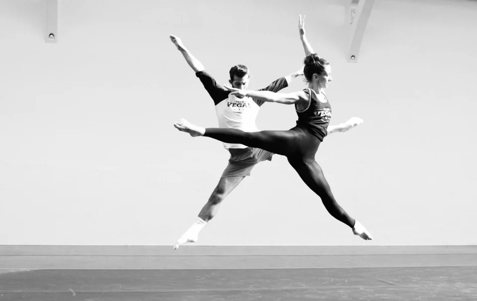 Amy and a dance partner leaping in a bright rehearsal studio